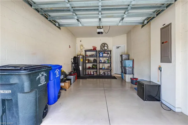 Garage with electric panel, water heater, black refrigerator, and concrete block wall