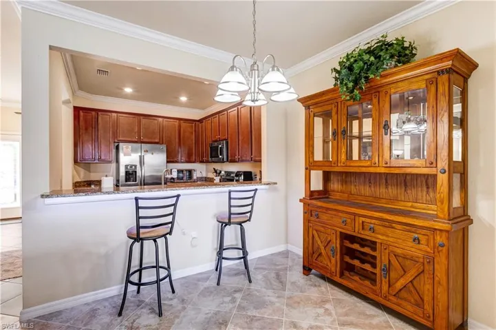 Kitchen with ornamental molding, a breakfast bar area, stainless steel appliances, decorative light fixtures, and light tile patterned floors