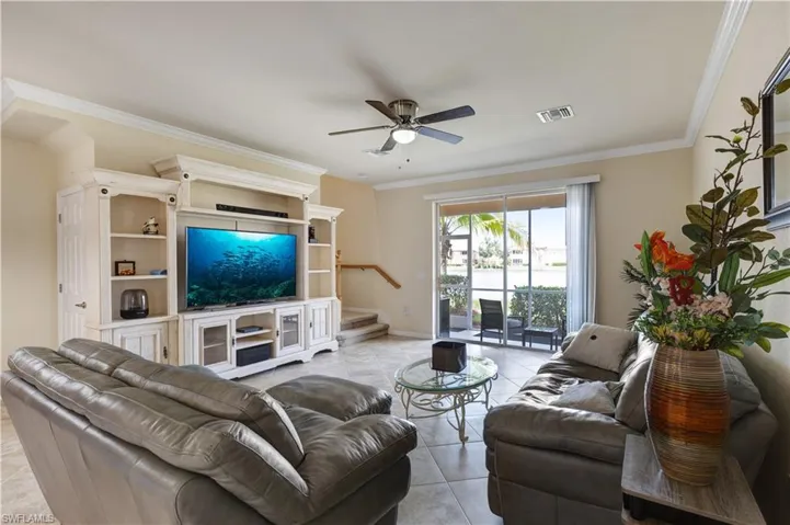 Living room featuring ornamental molding, stairs, light tile patterned floors, and a ceiling fan