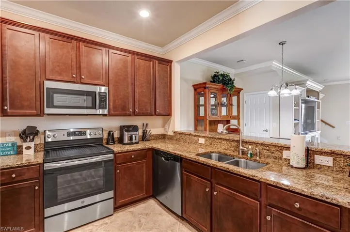 Kitchen with appliances with stainless steel finishes, ornamental molding, hanging light fixtures, light stone countertops, and a chandelier