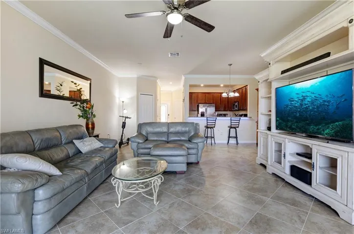 Living room featuring ornamental molding, light tile patterned floors, ceiling fan, a chandelier, and built in shelves