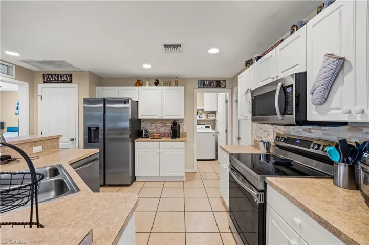 Kitchen featuring tasteful backsplash, white cabinets, stainless steel appliances, light tile patterned floors, and washer / dryer