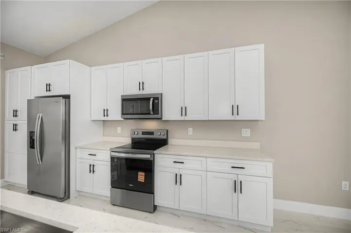 Kitchen featuring stainless steel appliances, white cabinetry, light stone counters, and lofted ceiling