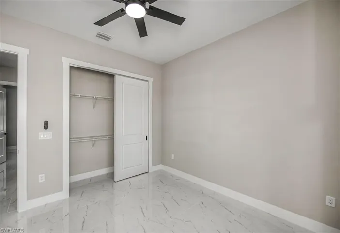 Unfurnished bedroom featuring ceiling fan, a closet, and light marble finish flooring