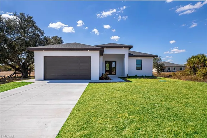 Prairie-style house featuring stucco siding, a front yard, driveway, an attached garage, and french doors