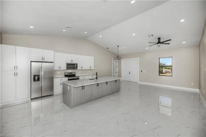 Kitchen featuring stainless steel appliances, a center island with sink, open floor plan, recessed lighting, and vaulted ceiling