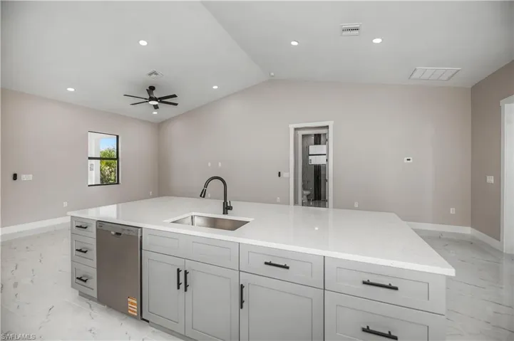 Kitchen with a center island with sink, stainless steel dishwasher, light stone countertops, light marble finish flooring, and recessed lighting
