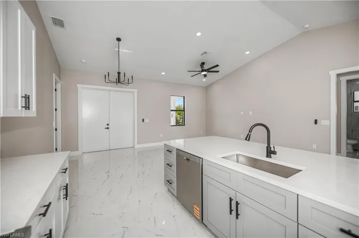 Kitchen with light stone counters, stainless steel dishwasher, light marble finish flooring, ceiling fan, and lofted ceiling