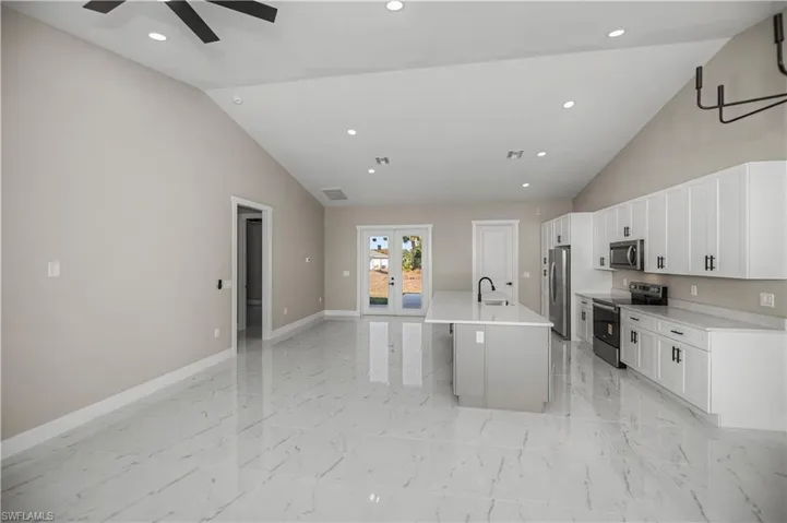 Kitchen with vaulted ceiling, stainless steel appliances, a kitchen island with sink, french doors, and open floor plan