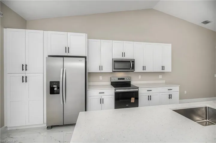 Kitchen featuring stainless steel appliances, light stone counters, white cabinetry, vaulted ceiling, and light marble finish flooring