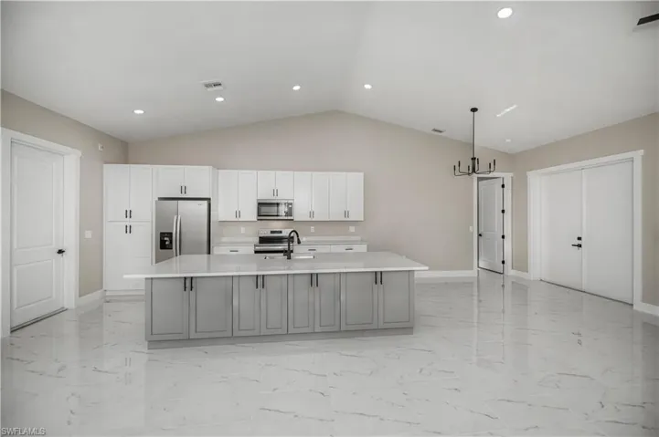 Kitchen with a kitchen island with sink, stainless steel appliances, a chandelier, light stone counters, and two tone cabinets