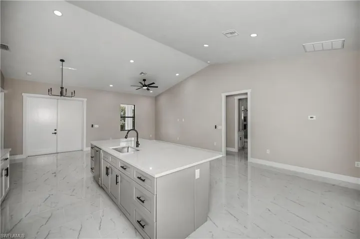 Kitchen featuring an island with sink, hanging light fixtures, light stone countertops, open floor plan, and ceiling fan