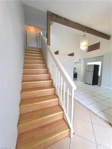 Staircase featuring wood-finish treads, white balusters, and a vaulted ceiling with exposed timber beams and a pendant light fixture