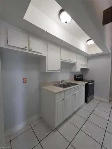 Kitchen featuring white cabinetry, solid-surface countertops, dual-basin stainless steel sink, tile flooring, and a recessed soffit with integrated lighting