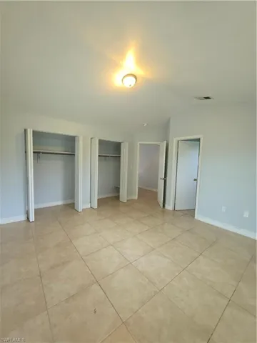 Neutral-toned ceramic tile flooring, two dual-door reach-in closets with integrated shelving, and vaulted ceilings