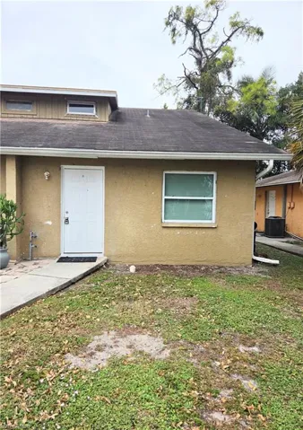 Exterior facade featuring stucco siding, a low-pitch roof, a single-entry door with a transom window, and a concrete walkway