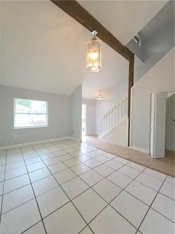 Vaulted ceilings featuring an exposed wood beam, ceramic tile flooring, and a decorative pendant light fixture, with a white staircase railing and built-in folding closet doors