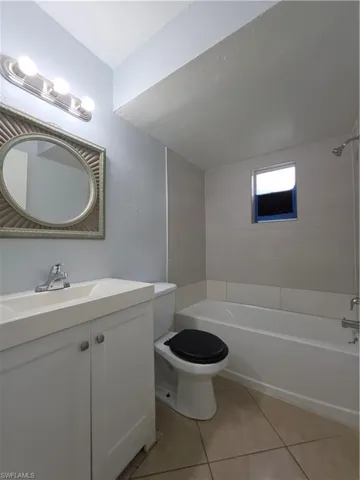 Bathroom featuring a white vanity with an integrated sink, polished chrome faucet, tile shower surround, and ceramic tile flooring