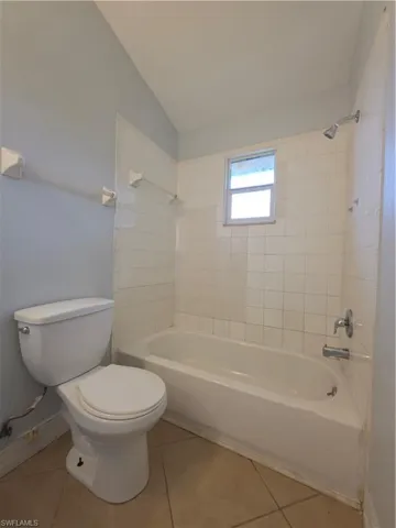 Full bathroom featuring a tub-shower combination with white wall tile, a window, a white porcelain toilet, and ceramic tile flooring