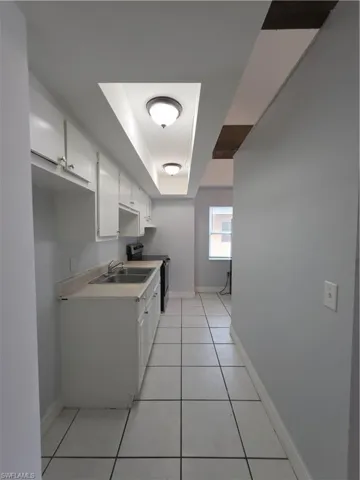 Kitchen featuring white cabinetry, light-toned solid surface countertops, a stainless steel double basin sink, recessed ceiling lighting, and tile flooring