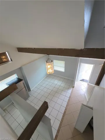 Vaulted ceilings featuring exposed wood beams, ceramic tile flooring, and a decorative pendant light fixture