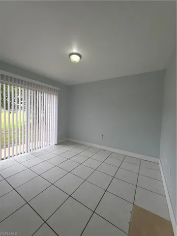 Neutral interior space featuring large-format square tile flooring, vertical window blinds, and a flush-mount ceiling light fixture