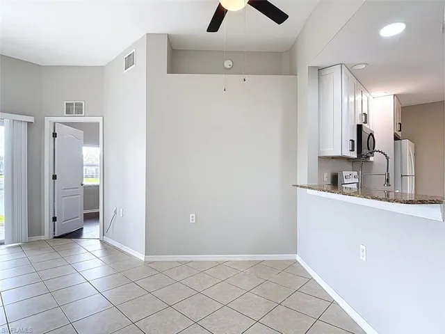 Kitchen featuring a ceiling fan, white cabinets, dark stone countertops, freestanding refrigerator, and light tile patterned floors
