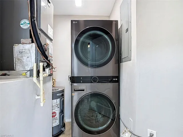 Laundry room featuring heating unit, stacked washer and dryer, water heater, and electric panel