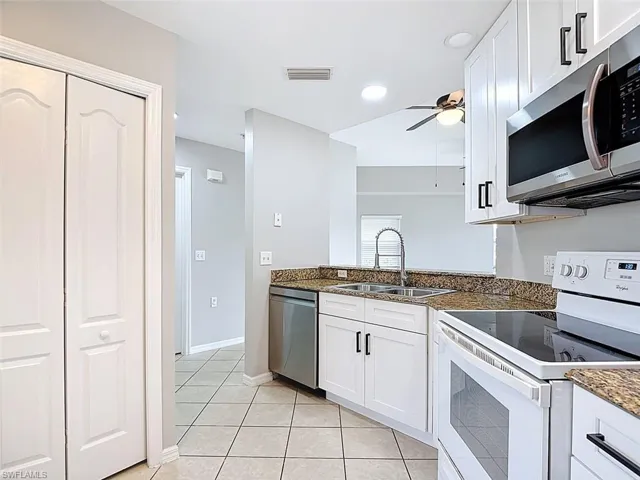 Kitchen featuring stainless steel appliances, dark stone counters, ceiling fan, white cabinetry, and light tile patterned floors
