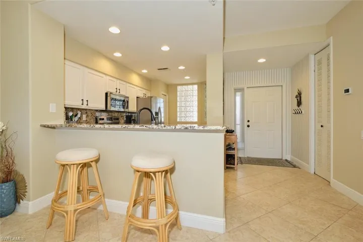 Kitchen featuring white cabinetry, kitchen peninsula, light stone countertops, and stainless steel appliances