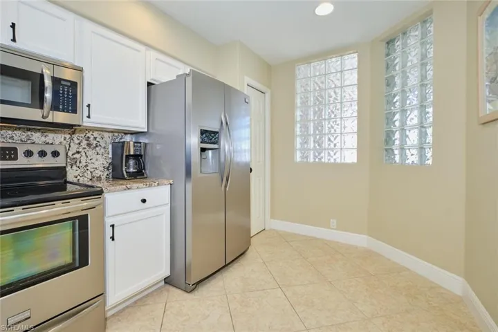 Kitchen with backsplash, light stone counters, white cabinetry, and stainless steel appliances