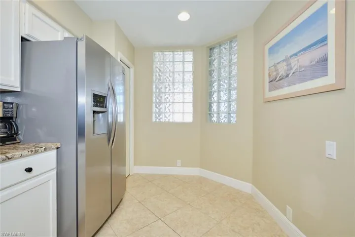 Kitchen featuring white cabinets, stainless steel fridge with ice dispenser, light tile patterned floors, and light stone counters