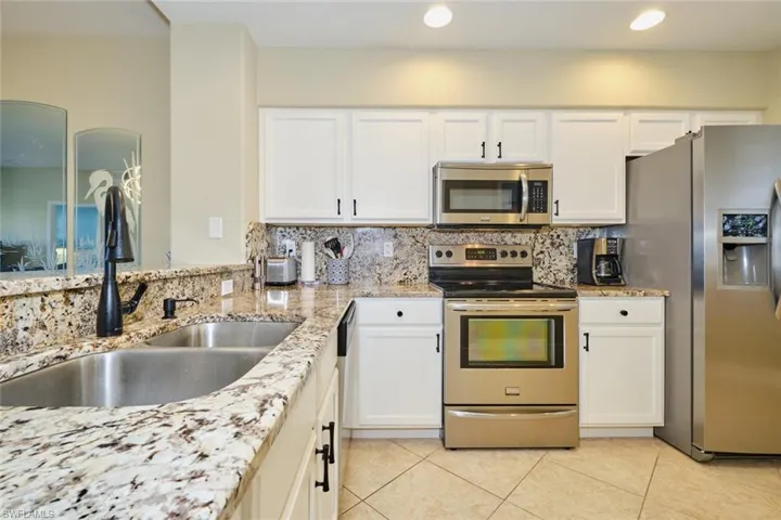 Kitchen with sink, light stone countertops, appliances with stainless steel finishes, tasteful backsplash, and white cabinetry