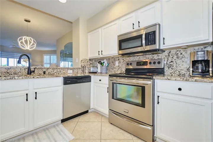 Kitchen with white cabinetry, sink, stainless steel appliances, decorative light fixtures, and light tile patterned floors