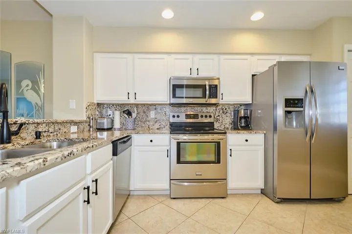 Kitchen with backsplash, light stone countertops, white cabinets, and stainless steel appliances