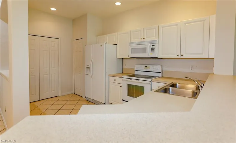 Kitchen with light tile patterned floors, white appliances, light countertops, white cabinetry, and recessed lighting