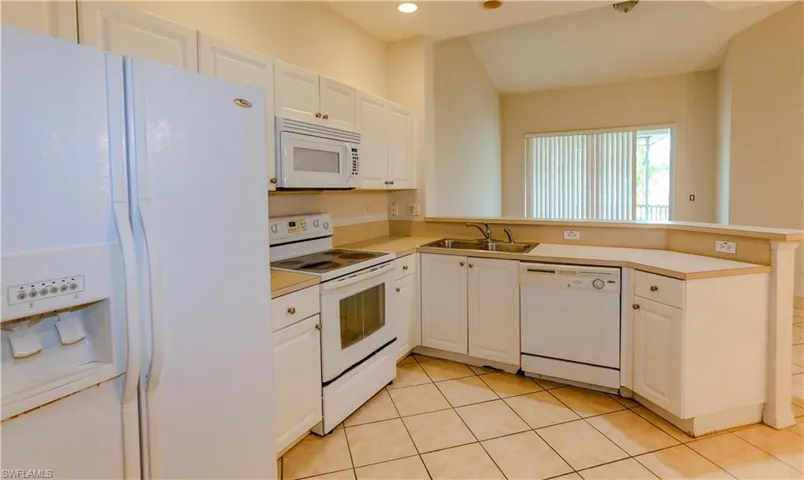 Kitchen with white appliances, white cabinets, a peninsula, light tile patterned floors, and light countertops