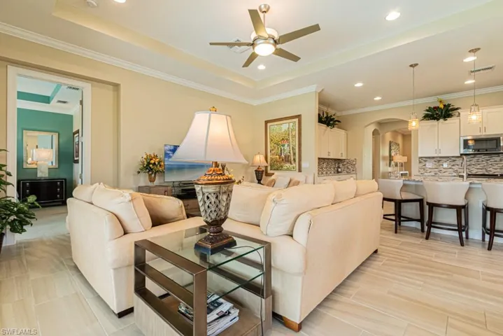 Living room featuring ceiling fan, a raised ceiling, light tile patterned floors, and crown molding