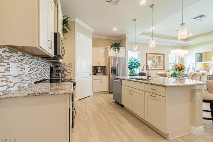 Kitchen featuring tasteful backsplash, hanging light fixtures, ornamental molding, and stainless steel appliances