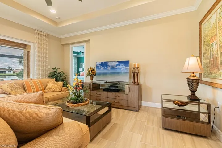 Tiled living room with ceiling fan, a raised ceiling, and ornamental molding