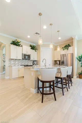Kitchen featuring appliances with stainless steel finishes, a center island with sink, crown molding, and hanging light fixtures