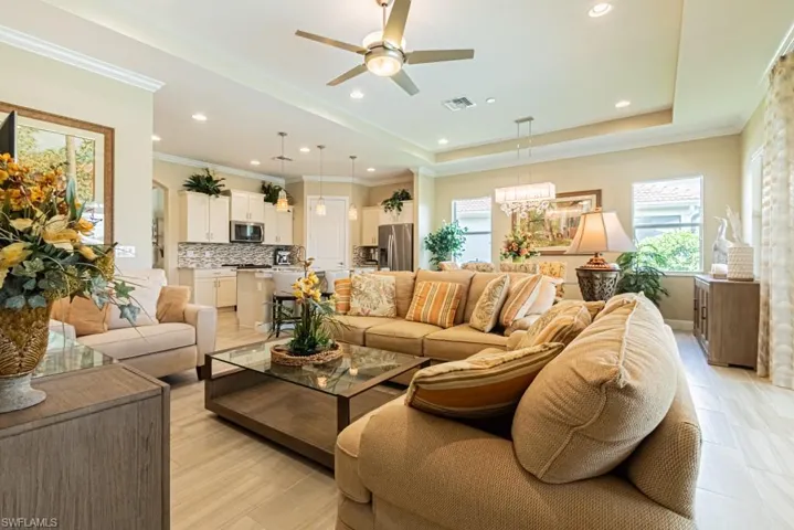 Living room with a raised ceiling, ceiling fan with notable chandelier, and ornamental molding