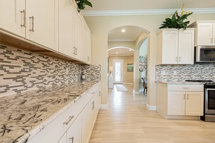 Kitchen featuring appliances with stainless steel finishes, crown molding, light stone countertops, and tasteful backsplash