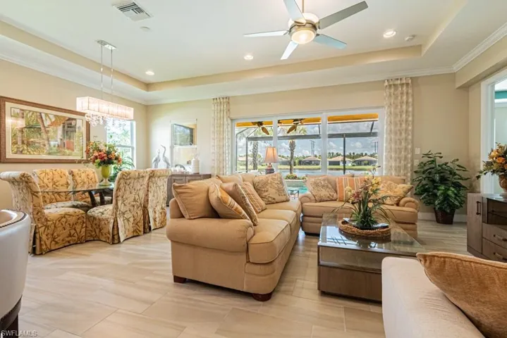Tiled living room featuring ceiling fan, a raised ceiling, and a wealth of natural light