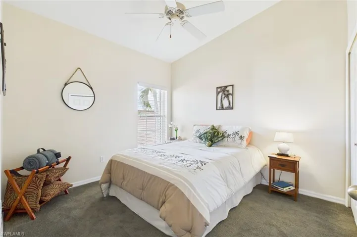 Bedroom with dark colored carpet, lofted ceiling, and a ceiling fan