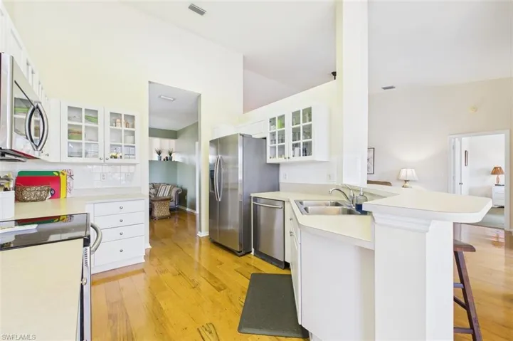 Kitchen with glass insert cabinets, white cabinets, stainless steel appliances, a peninsula, and light countertops