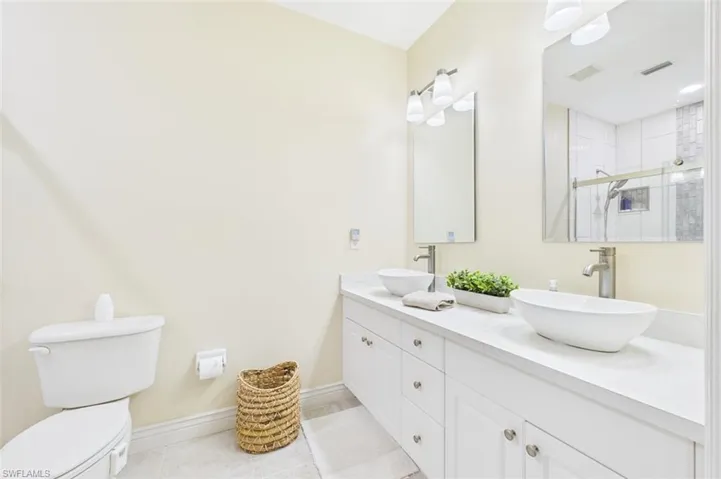 Full bathroom with double vanity, light tile patterned floors, and an enclosed shower