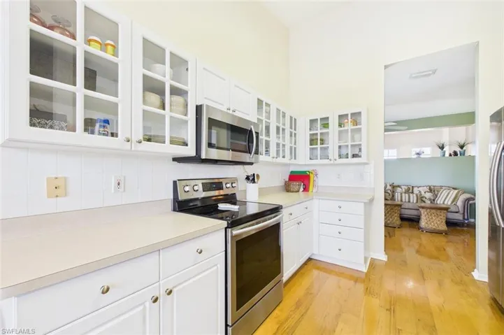 Kitchen featuring appliances with stainless steel finishes, tasteful backsplash, light countertops, white cabinets, and glass insert cabinets