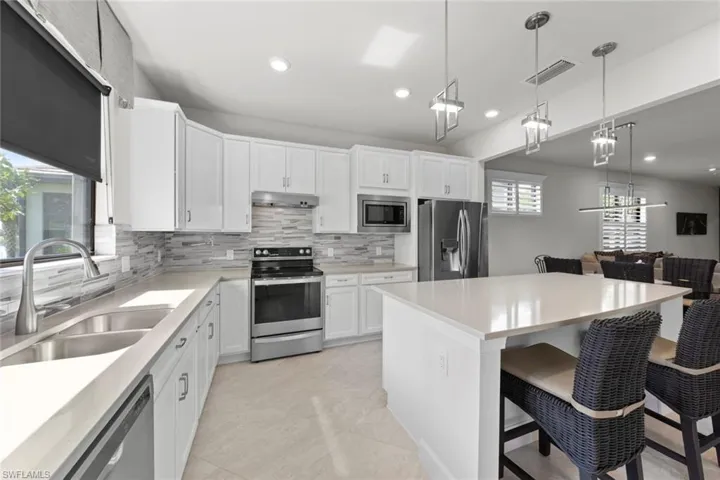 Kitchen featuring a breakfast bar, sink, white cabinets, backsplash, and appliances with stainless steel finishes
