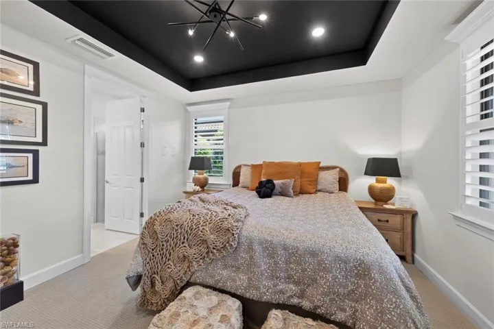 Carpeted bedroom featuring a raised ceiling and a notable chandelier